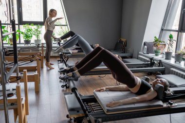 Beyaz bir kadın grubu parlak bir stüdyoda antrenörle pilates reformcuları üzerinde egzersiz yapıyor. Onların çalışmaları modern bir fitness ortamında çekirdek kuvveti ve esnekliği üzerine odaklanır..