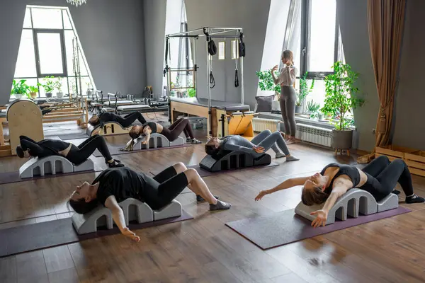 Omurga düzelticisi üzerinde egzersiz yapan bir grup kadın. Beden eğitimi için pilates stüdyosu makinesi. Formda, sağlıklı ve güçlü özgün bir vücut. Fitness konsepti