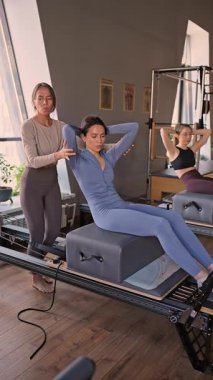 Kadın, göğüs ve sırt kasları için Pilates Reformcusu üzerinde rotasyon egzersizi yapıyor. Kararlılıkla esneklik, güç ve kontrole odaklanıyor..
