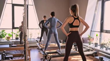 Genç beyaz kadınlar parlak bir stüdyoda pilates reformcuları üzerinde egzersiz yapıyorlar. Onların çalışmaları modern bir fitness ortamında çekirdek kuvveti ve esnekliği üzerine odaklanır..