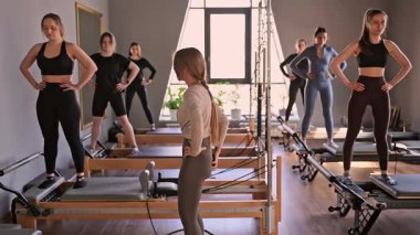 Genç beyaz kadınlar parlak bir stüdyoda pilates reformcuları üzerinde egzersiz yapıyorlar. Onların çalışmaları modern bir fitness ortamında çekirdek kuvveti ve esnekliği üzerine odaklanır..