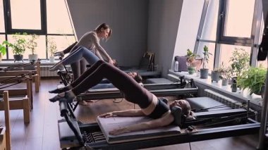 Bir grup kadın, kalça ve pelvise odaklanan, güneş ışığı altında reformist bir yatak makinesinde Glute Köprüsü 'nü çalıştırıyor.