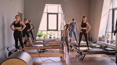 Genç beyaz kadınlar parlak bir stüdyoda pilates reformcuları üzerinde egzersiz yapıyorlar. Onların çalışmaları modern bir fitness ortamında çekirdek kuvveti ve esnekliği üzerine odaklanır..