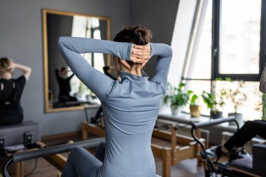 Kadın, göğüs ve sırt kasları için Pilates Reformcusu üzerinde rotasyon egzersizi yapıyor. Kararlılıkla esneklik, güç ve kontrole odaklanıyor..