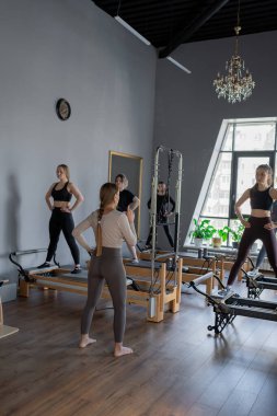 Genç beyaz kadınlar parlak bir stüdyoda pilates reformcuları üzerinde egzersiz yapıyorlar. Onların çalışmaları modern bir fitness ortamında çekirdek kuvveti ve esnekliği üzerine odaklanır..