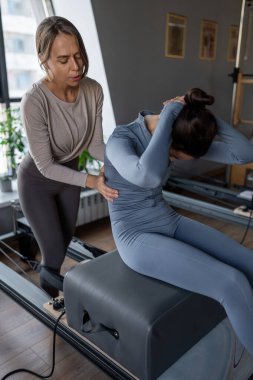 Kadın, göğüs ve sırt kasları için Pilates Reformcusu üzerinde rotasyon egzersizi yapıyor. Kararlılıkla esneklik, güç ve kontrole odaklanıyor..