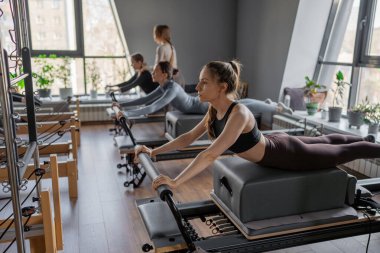 Kuğu egzersizi yapan kadınlar, göğüs ve sırt kasları için Pilates Reformcusu, esneklik, güç ve kararlılıkla kontrol üzerine odaklanıyorlar.