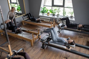 Bir grup kadın, kalça ve pelvise odaklanan, güneş ışığı altında reformist bir yatak makinesinde Glute Köprüsü 'nü çalıştırıyor.