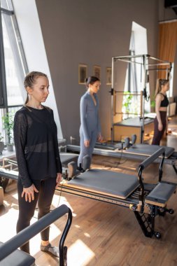 Genç beyaz kadın pilates salonunun parlak stüdyosunda egzersiz yapıyor. Onların çalışmaları modern bir fitness ortamında çekirdek kuvveti ve esnekliği üzerine odaklanır.
