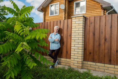 Huzurlu bir an, yemyeşil bir bahçede, yıpranmış ahşap bir çitin yanında huzur içinde duran bir kadını yakalar.