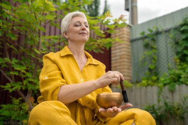 Sakin bir açık hava ortamında, dikkat çekmek için bir şarkı kasesi kullanarak sakin bir meditasyon pratiği yapın.