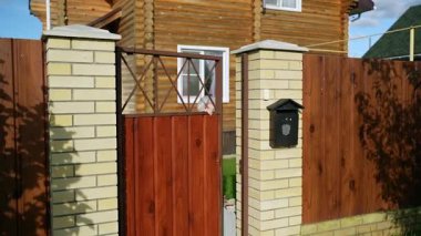 Bir kadın gururla duruyor büyüleyici ahşap evinde, yemyeşil ve yukarıda güneşli bir gökyüzü ile çevrili.