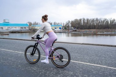 Şık bir kadın, sakin bir su vücuduyla zarif bir şekilde bisiklete biniyor. Şatafatlı bir spor salonu ve canlı bir açık hava yaşam tarzı.