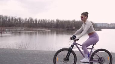 Parkta ağaçların arkasında bisiklete binen genç bir kadın. Modayı takip eden aktif bir kız doğaya zaman ayırıyor. Yan görüş. Yüksek kalite fotoğraf