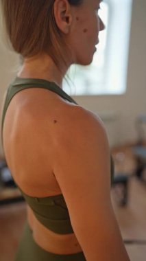 A woman in activewear does pilates exercises for the chest, arms and back muscles with a reformer machine in a sunlite studio, committed to her workout routine