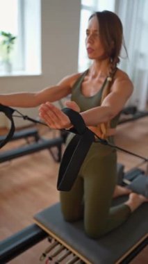 A woman in activewear does pilates exercises for the chest, arms and back muscles with a reformer machine in a sunlite studio, committed to her workout routine