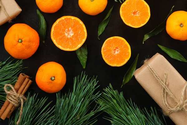 Christmas, New Year\'s winter background with juicy tangerines on a dark wooden table. Top view of citrus fruits, gifts, pine branches and cinnamon in tubules. Festive background