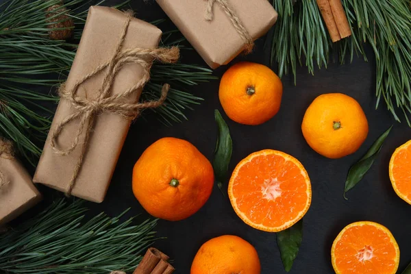 Christmas, New Year\'s winter background with juicy tangerines on a dark wooden table. Top view of citrus fruits, gifts, pine branches, close-up photo. Festive background