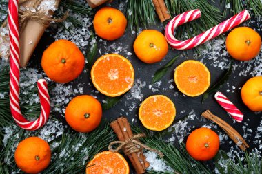 Kesilmiş bir Noel arkaplanı ve tüm mandalinalar karlı bir masanın üstünde, manzaralı. Citrus meyveleri, şekerler, hediyeler, çam ağaçları ve tarçın