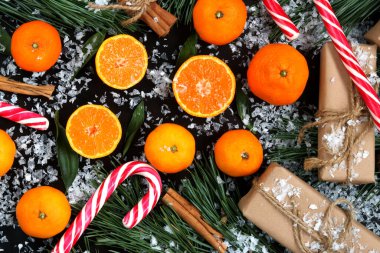 Noel arkaplanlı, mandalinalı, karlı karanlık bir masada, manzaralı. Meyveler, şekerler, hediyeler, çam ağaçları ve tarçın. Neşeli arkaplan