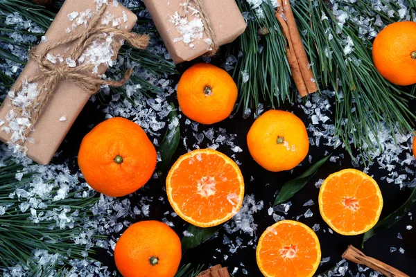 Snow-covered Christmas composition, background with cut and whole tangerines, top view. Citrus fruits, gifts, pine branches and cinnamon