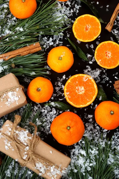 Snow-covered Christmas composition, background with cut and whole tangerines, top view. Citrus fruits, gifts, pine branches and cinnamon