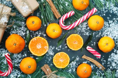 Noel arkaplanlı, mandalinalı, karlı karanlık bir masada, manzaralı. Meyveler, şekerler, hediyeler, çam ağaçları ve tarçın. Kartpostalı karşıla, yeni yıl için tebrikler.