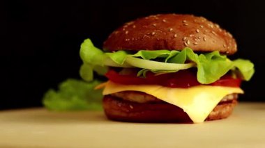 Burger with cutlet, melted cheese, salad and vegetables. Burger and fresh vegetables: lettuce and tomatoes. Fast food, rotating in front of camera on dark background, close-up view