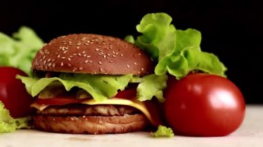 Juicy burger with tomatoes and lettuce. Smooth camera movement. Cheeseburger and fresh vegetables on a dark background. Fast food closeup