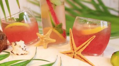 Kokteylli yaz kompozisyonu, limonatalı bardaklar ya da sahilde alkol. Kumda, denizyıldızında ve palmiye yapraklarında kokteyller