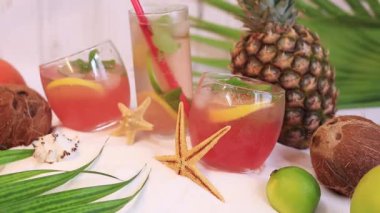 Kokteylli yaz kompozisyonu, limonatalı bardaklar ya da sahilde alkol. Beyaz kum, denizyıldızı, palmiye yaprakları ve tropikal meyveler üzerinde kokteyller. Plaj tatili