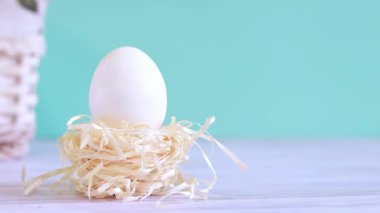 Easter egg in a decorative nest. Clean white egg, easter composition. Slowly receding video on a blue background