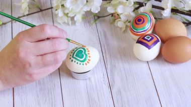Easter eggs. Preparation for the holiday, paint eggs with paints, draw hearts. Female hands with brush and egg, easter composition, coloring lesson