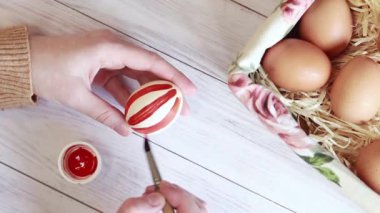 Striped Easter egg. Color the egg with red paints, top view of female hands with an egg and a brush. Preparing for the holiday, handmade