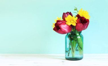 Bouquet of spring flowers with tulips in a glass jar. Spring flowers on a blue background. Flowers with empty space nearby. Photo to create postcards