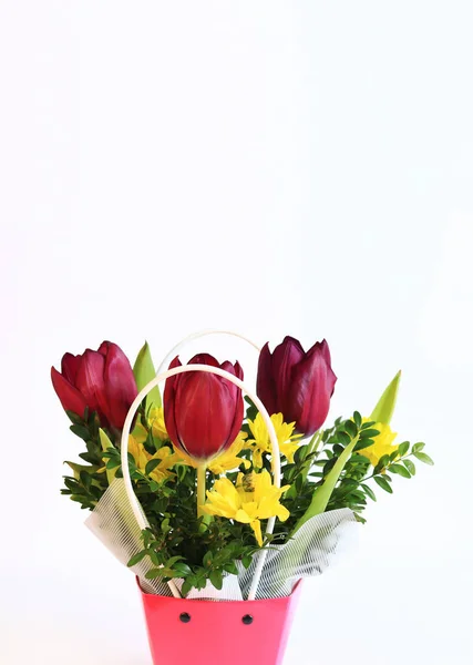 Bouquet of spring flowers with tulips in a pink cardboard basket. Spring flowers on a white background. Flowers with empty space nearby. Photo to create postcards