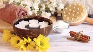 SPA kompozisyonu, yakın video. Mumlar suda. İçinde mumlar, çiçekler, tarçın tüpleri, masaj fırçası ve tuz olan hindistan cevizi kasesi. Spa prosedürü ya da masaj için hazırlık, hafif rüzgar