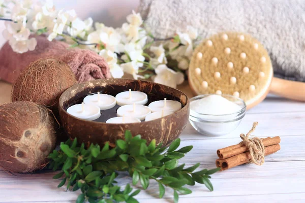 Suyun içinde mumlar olan spa kompozisyonu. İçinde mumlar, çiçekler, tarçın tüpleri, masaj fırçası ve tuz olan hindistan cevizi kasesi. Spa prosedürü ya da masaj için hazırlık. Dinlen.