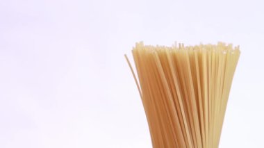 Pişmemiş bir spagetti paketi hafif bir arka planda döner. Yan görünüş, makarna yakın plan, sol tarafında fotokopi alanı var.