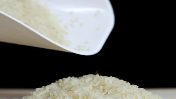 米粒从塑料白色勺子中溢出 煮熟了很久的米饭 稻谷在黑色的背景上堆成一堆 — 图库视频影像