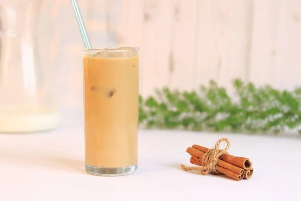 Ice latte. Coffee with ice and milk against the backdrop of a light kitchen, cinnamon, carafe with milk and a green plant. Stir the drink with a straw