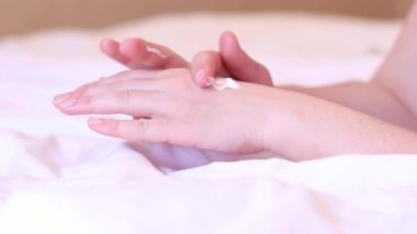 Kız, kremi cilde çarşafın arka planına sürmüş. Yaşlanma önleyici cilt bakım ürünleri. Eller yakın çekim, kız nemlendirici sürüyor ve yumuşaklık için eline masaj yapıyor.