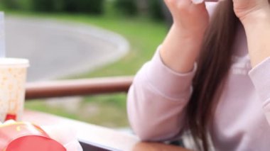 Kyiv, Ukrayna - 11 Mayıs 2023: Kız bir McDonald 's hamburgeri yiyor. Fast food restoranında hamburger yiyen bir kadın. McDonald 's Corporation dünyanın en büyük fast food restoranıdır. Açık hava masasında yemek. Seçici odak