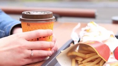 Kyiv, Ukrayna - 11 Mayıs 2023: McDonald 's' dan fast food. Kahve ve patates kızartmasıyla yakın plan kadın eli. Açık hava masasında yemek. Seçici odak