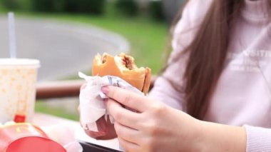 Kyiv, Ukrayna - 11 Mayıs 2023: Kız bir McDonald 's hamburgeri yiyor. Fast food restoranında hamburger yiyen bir kadın. McDonald 's Corporation dünyanın en büyük fast food restoranıdır. Açık hava masasında yemek. Seçici odak