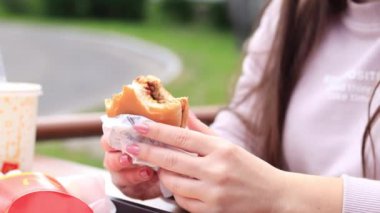 Kyiv, Ukrayna - 11 Mayıs 2023: Kız bir McDonald 's hamburgeri yiyor. Fast food restoranında hamburger yiyen bir kadın. McDonald 's Corporation dünyanın en büyük fast food restoranıdır. Açık hava masasında yemek. Seçici odak