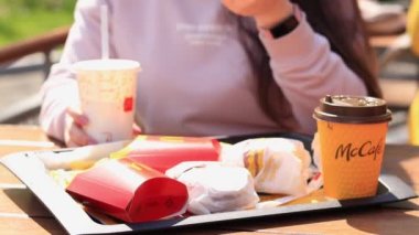 Kyiv, Ukrayna - 11 Mayıs 2023: Kız McDonalds 'da açık hava masasında yemek yiyor. Kız fast food yiyor. Kadın eli patates kızartması alır. McDonald 's Corporation dünyanın en büyük fast food restoranıdır.