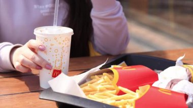 Kyiv, Ukrayna - 11 Mayıs 2023: Kız McDonalds 'da açık hava masasında yemek yiyor. Kız fast food yiyor. Kadın eli patates kızartması alır. McDonald 's Corporation dünyanın en büyük fast food restoranıdır.
