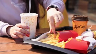 Kyiv, Ukrayna - 11 Mayıs 2023: Kız McDonalds 'da açık hava masasında yemek yiyor. Kız fast food yiyor. Kadın eli patates kızartması alır. McDonald 's Corporation dünyanın en büyük fast food restoranıdır.