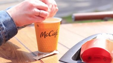Kyiv, Ukrayna - 11 Mayıs 2023: Kadın bir McDonald 's kahvesine şeker döker. Kızın elleri bardaktaki bir içeceğe şeker döküyor. McDonald 's' da anlık kahve. McDonalds restoranında sarı McCafe kapuçino.